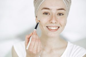 pale woman with hair in towel using a makeup brush